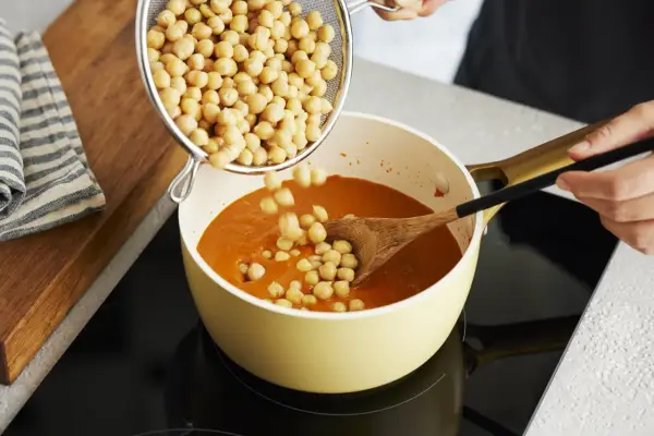Kichererbsen werden in einen Topf mit Curry gegeben. Perfekt für die Zubereitung von Kichererbsen-Curry zum Einfrieren.