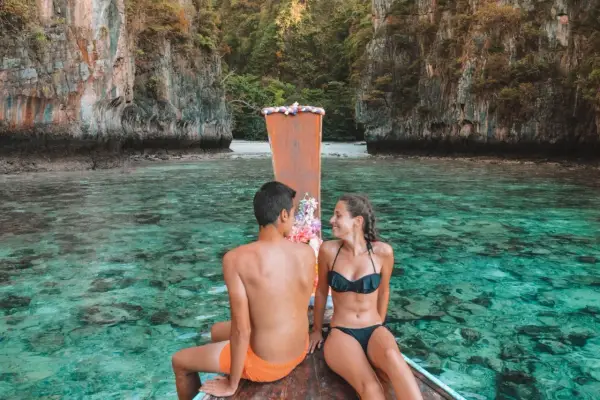 Pareja en bote de madera, aguas cristalinas y acantilados. Un destino ideal para saber donde viajar en enero.