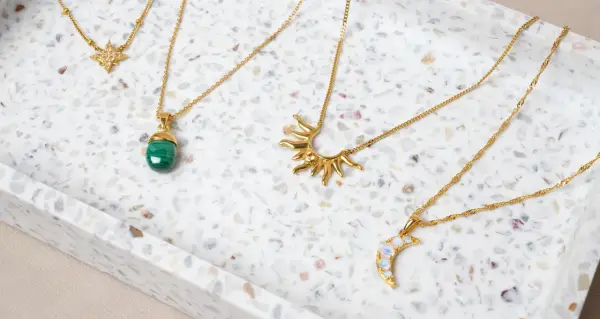 Fyra guldfärgade halsband med olika hängen: en stjärna, en grön sten, en sol och en måne. Vilken kristall passar mig?