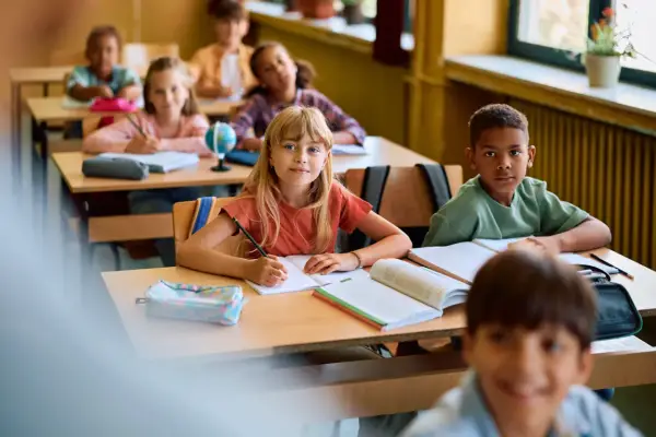 Dzieci w klasie skupione na lekcji. Uczennica pisze w zeszycie, obok niej leży piórnik. To pokazuje, co na koncentrację u dzieci: nauka i zaangażowanie.