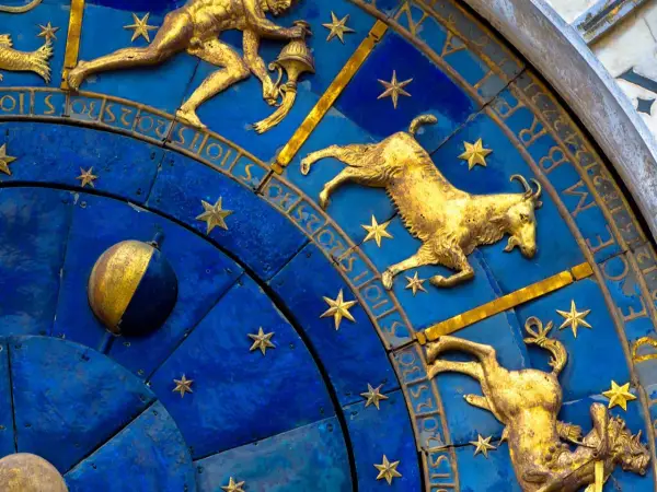Złote figury Koziorożca i innych znaków zodiaku na niebieskiej tarczy zegara. 19 stycznia to czas Koziorożca.