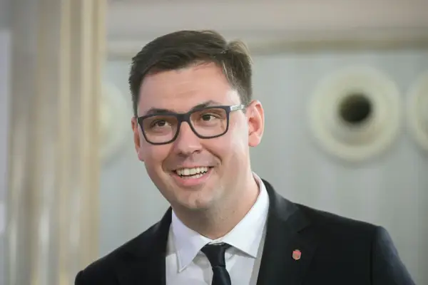 Uśmiechnięty Konrad Frysztak w okularach, w garniturze. Jego wykształcenie pozwala mu na pewność siebie w każdej sytuacji.