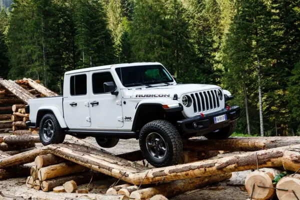 Biały jeep pickup Rubicon pokonuje przeszkodę z bali drewna w lesie.