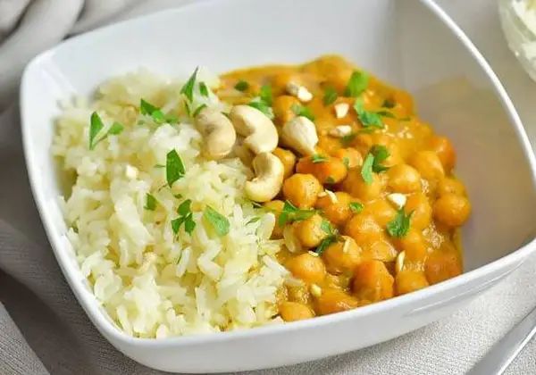 Curry de garbanzos cremoso con arroz blanco y anacardos en un cuenco blanco.