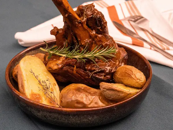 Un plat appétissant de souris d'agneau confite, tendre et savoureuse, accompagnée de pommes de terre rôties et d'une touche de romarin frais.