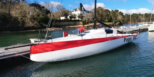 Le voilier Pogo RC, blanc et rouge, est amarré à un ponton. Une personne en blouson rouge est à bord.