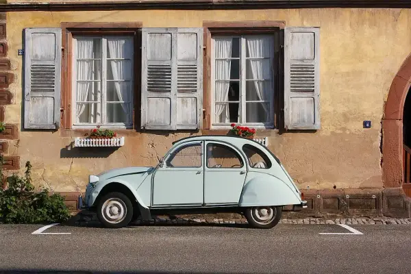 Jasnoniebieski, zabytkowy Citroen 2CV, jeden z tych klasycznych, francuskich modele stare, stoi przed kamiennym domem z drewnianymi okiennicami.