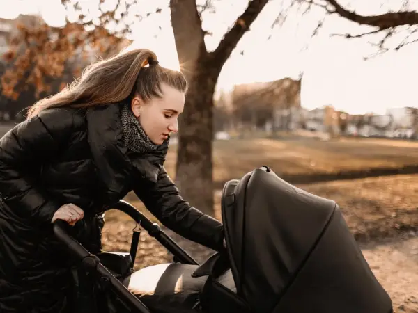 Mama przygotowuje malucha na spacer w 15 stopniach. Ciepła kurtka i szalik to podstawa, by zapewnić komfort dziecku w wózku.