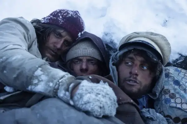 Tre uomini stremati nel gelo, un'immagine che evoca le recensioni de "La società della neve", la lotta per la sopravvivenza.