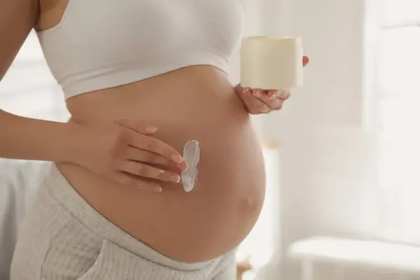 Kobieta w ciąży smaruje brzuch kremem. Delikatna pielęgnacja skóry, jak aloes w ciąży, to ważny element dbania o siebie.