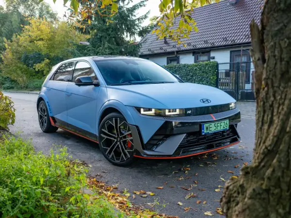 Niebieski Hyundai Ioniq 5 N z czerwonymi akcentami stoi na tle domu i drzew.