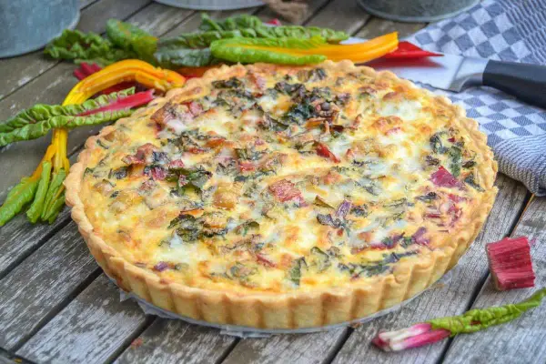 Herzhafte Quiche mit buntem Mangold und knusprigem quiche teig auf Holztisch, garniert mit frischem Mangold.