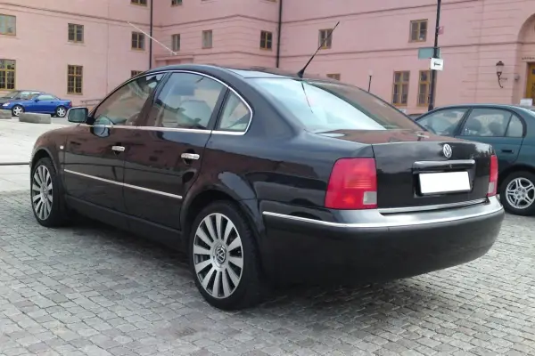 Svart Passat W8 parkerad på kullerstensgata framför en rosa byggnad.