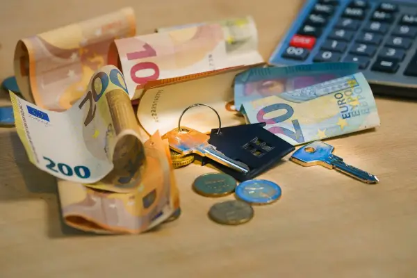 Clés, pièces et billets d'euros sur une table en bois. Calculatrice en arrière-plan. Le prix pose carrelage m2 est une préoccupation.