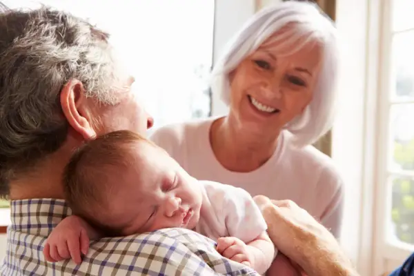 Los abuelos paternos sonríen mientras el abuelo sostiene al bebé dormido en su hombro.