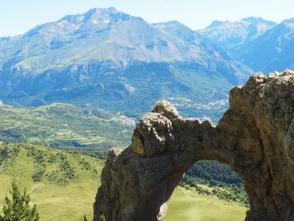 Arco natural en el valle de Tena, con vistas a montañas y un pueblo. Imagina a niños explorando este paisaje.