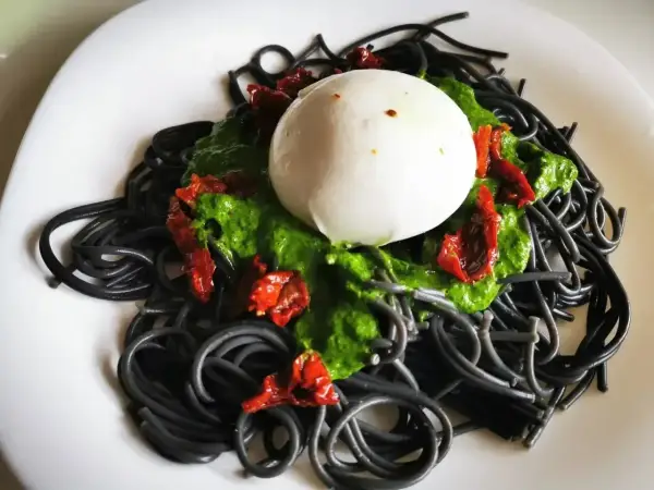 Czarny makaron z zielonym pesto, suszonymi pomidorami i kulką mozzarelli. Wygląda apetycznie!