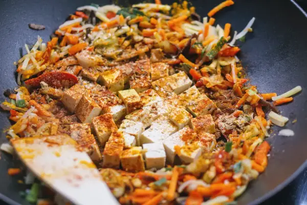Kawałki tofu i kolorowe warzywa po chińsku smażą się na patelni wok, przyprawione kurkumą i papryką.
