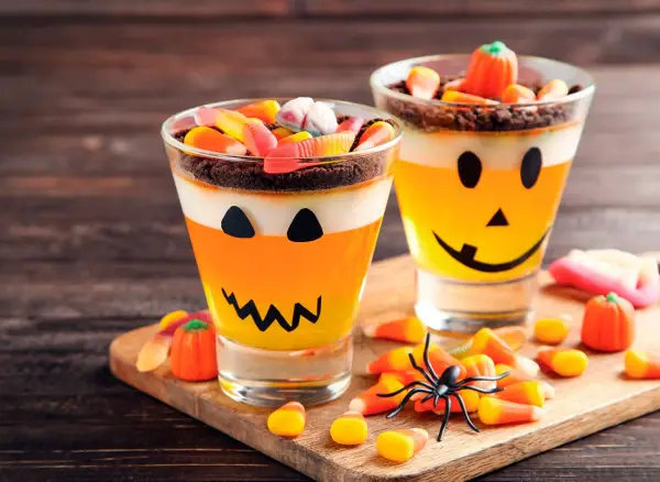 Deliciosa gelatina Halloween para niños, con capas de naranja y blanco, decorada como calabaza y cubierta de dulces.