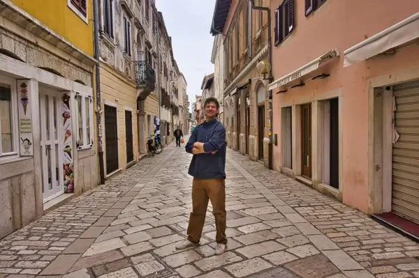 Mann steht in einer Gasse mit Kopfsteinpflaster in Poreč. Ein Eisgeschäft und Boutiquen säumen die Straße. Ein toller Ort für Poreč Geheimtipps.
