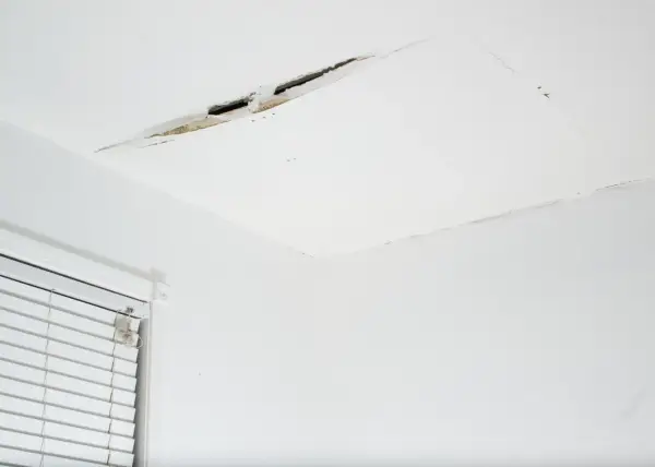 Widoczny pęknięcie na suficie w bloku, odsłaniające fragmenty konstrukcji. Obok okno z białymi żaluzjami.