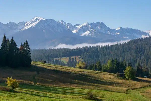 Gubałówka atrakcje: malowniczy widok na Tatry, zielone wzgórza, lasy i kilka drewnianych budynków.