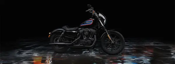 Czarny Harley-Davidson Iron 1200 z kolorowym paskiem na baku, stojący na mokrej, błyszczącej nawierzchni.