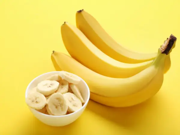 Pytanie: czy banany są kaloryczne? Na żółtym tle pęczek żółtych bananów i miseczka z plasterkami banana.
