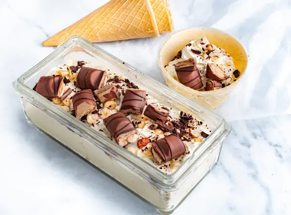 Lody Kinder Bueno w pojemniku i wafelku, posypane orzechami i czekoladą.