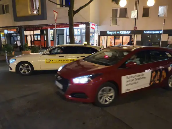 Ein weißes Taxi und ein rotes Auto mit Uber-Werbung stehen nebeneinander. Der Unterschied über Taxi ist die moderne Alternative.