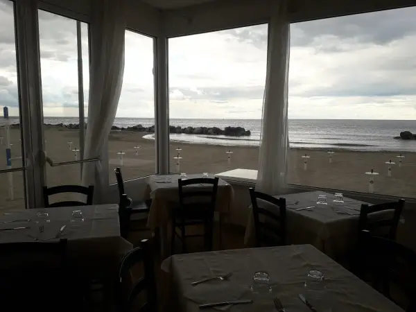 Tavoli apparecchiati in un ristorante con vista sulla spiaggia di Misano durante la bassa marea.