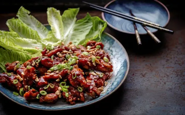 En tallrik med krispiga, glaserade kycklingvingar, toppade med hackade jordnötter och salladslök. Serveras med krispiga salladsblad. En utsökt koreansk matupplevelse.