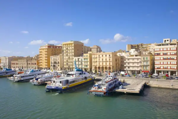 Ferries docked in a harbor, with buildings lining the waterfront. Wondering if you can drive to Sicily? These ferries might be your answer!