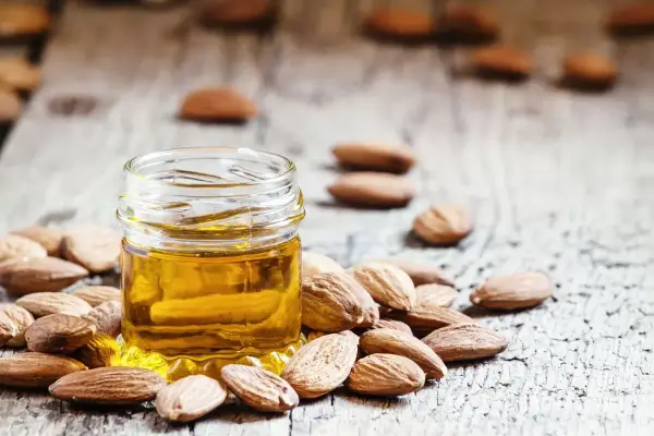 Un frasco de aceite de almendras para la cara rodeado de almendras enteras sobre una superficie de madera rústica.