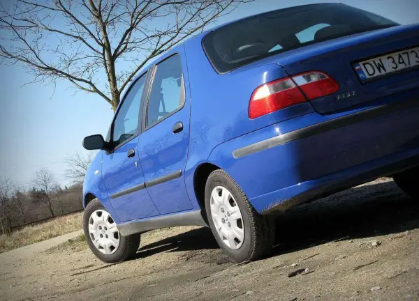 Niebieski Fiat Albea na tle drzew i błękitnego nieba.