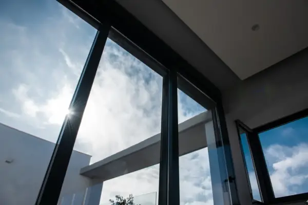 El sol brilla a través del vidrio guardian, iluminando un cielo azul con nubes blancas.