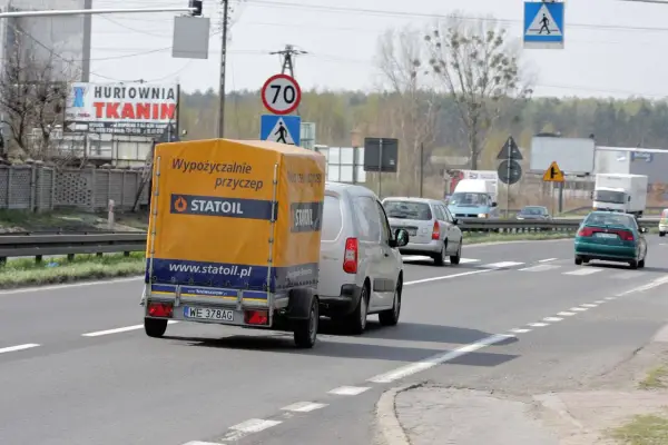 Na drodze widać przyczepę z napisem "Wypożyczalnie przyczep Statoil". Znak ograniczenia prędkości wskazuje 70 km/h, co sugeruje, ile autobus może jechać na autostradzie w takich warunkach.