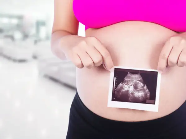 Ciężarna kobieta trzyma zdjęcie USG płodu na tle rozmazanego wnętrza.