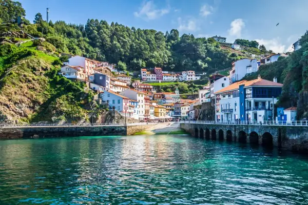 Un pintoresco pueblo costero con **5 villas** coloridas apiladas en una colina verde, frente a un mar turquesa.