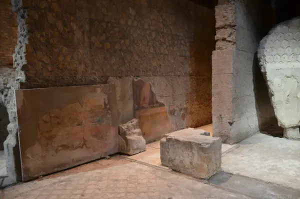 Vestiges d'une fresque murale dans la maison d'Auguste à Rome, avec des blocs de pierre et des murs en ruine.