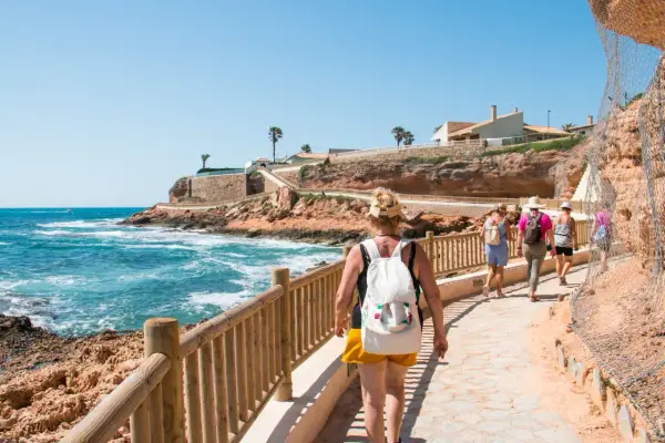 Paseo por la costa en cala capitan. Turistas caminan por un sendero con vistas al mar azul y acantilados rojizos.