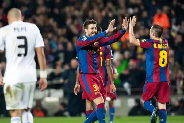 Piłkarze Barcelony, Piqué i Iniesta, świętują bramkę. Na pierwszym planie zawodnik w białej koszulce z numerem 3.