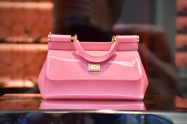 Różowa, lakierowana torebka od Dolce & Gabbana, symbol luksusowych marek torebek, błyszczy na tle sklepu.