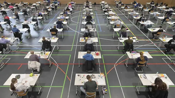 Viele Schüler sitzen in einer Sporthalle an Tischen, um zum Abitur zu schreiben.