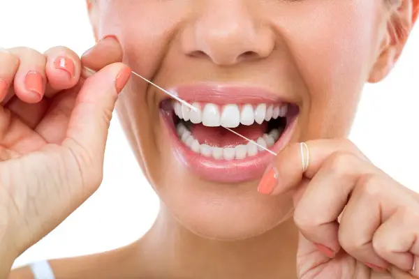 Donna sorride mentre usa il filo interdentale cerato per pulire i suoi denti bianchi e sani.