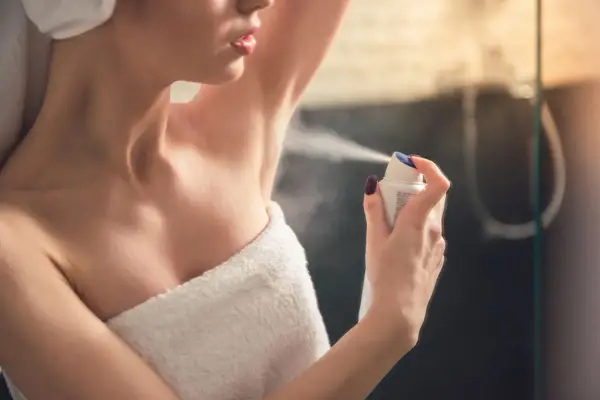 Kobieta aplikuje antyperspirant pod pachę, pokazując różnicę między dezodorantem a antyperspirantem.