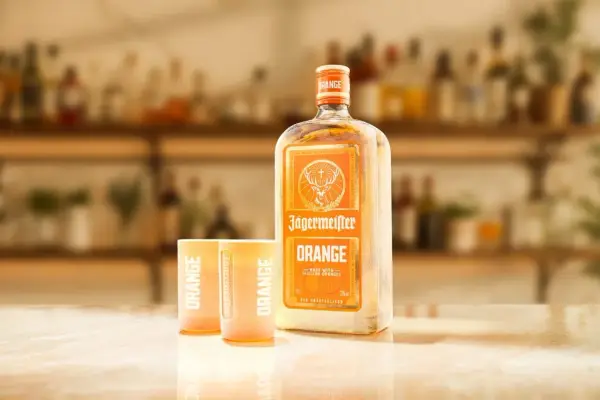 Butelka Jägermeister Orange i dwa kieliszki z napisem "ORANGE" na blacie. Idealny zestaw na letnie wieczory.