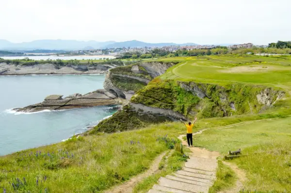 Persona con los brazos en alto en un acantilado verde, contemplando el mar y la costa. ¡Ideas para que ver en Cantabria en 4 días!