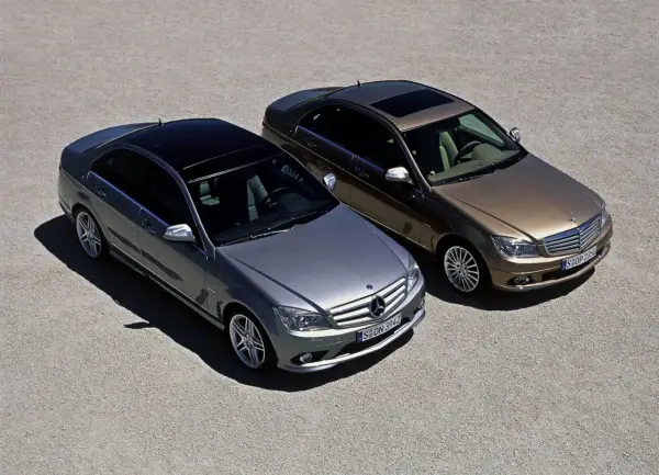 Dwa Mercedesy klasy C W204, jeden srebrny, drugi brązowy, stoją obok siebie na żwirowym placu.
