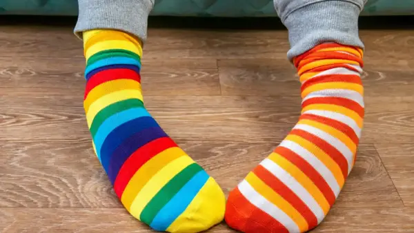 Kolorowe skarpetki w paski, tęczowe i pomarańczowo-białe, leżą na drewnianej podłodze. Jak doprać kolorowe skarpetki?